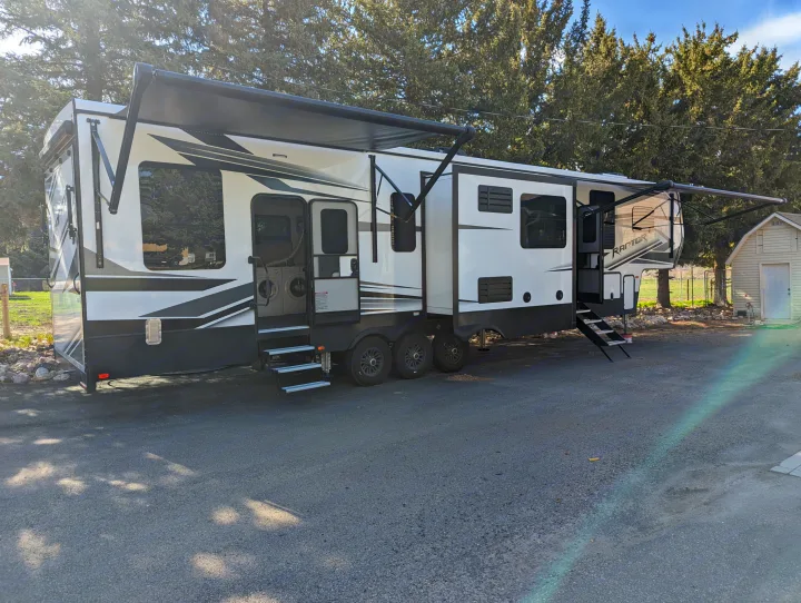Spacious white/black RV fifth-wheel with extended awnings & slides, showing washer/dryer inside. Perfect for your RV rental!. Keystone Raptor 2021