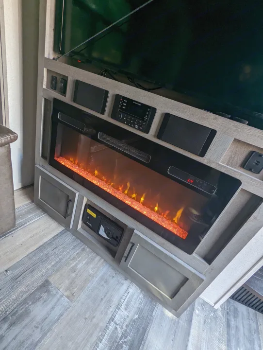 RV rental interior: glowing electric fireplace, TV, integrated stereo, USB ports, and wood-look floor.. Keystone Raptor 2021