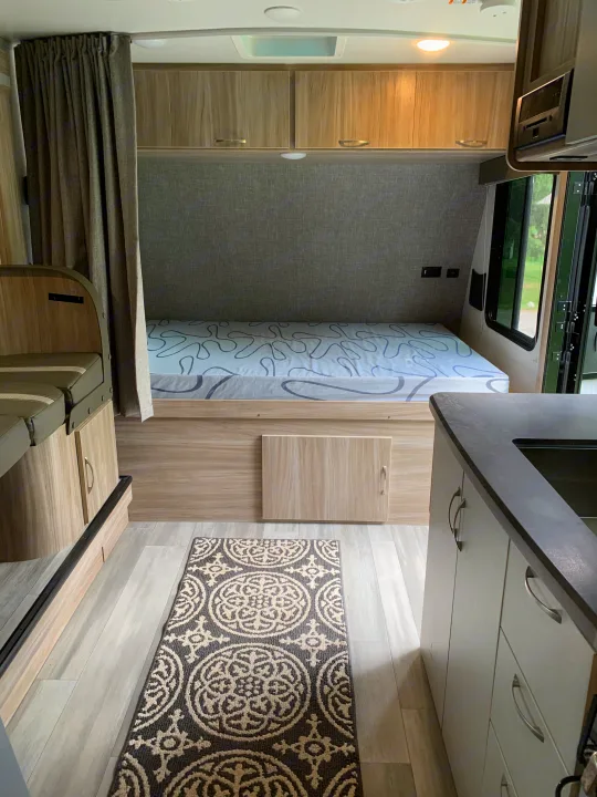 Inside an RV rental: a compact bedroom with a bed & storage, plus a glimpse of the kitchen and dining area.. Winnebago Micro Minnie 2021
