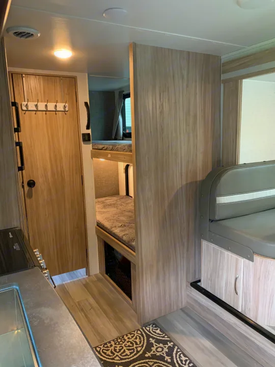 RV rental interior showcasing compact living with bunk beds, a small kitchen, and a dining booth. Light wood accents provide a modern feel.. Winnebago Micro Minnie 2021