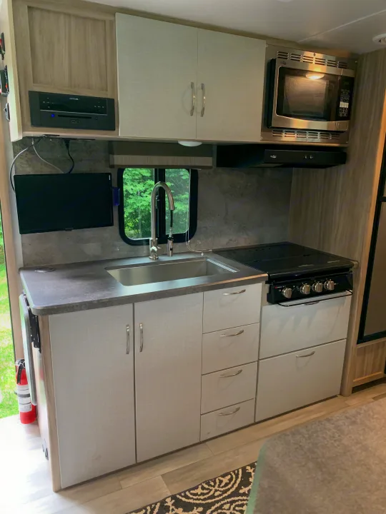 Well-equipped RV rental kitchen featuring a stainless steel sink, stove, microwave, ample storage cabinets, and a small TV.. Winnebago Micro Minnie 2021