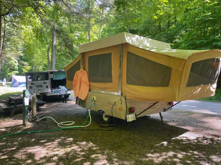 RV rental pop-up camper set up in a shady, wooded campsite with utility hookups. Ideal for outdoor adventures.. Coleman Other 1983