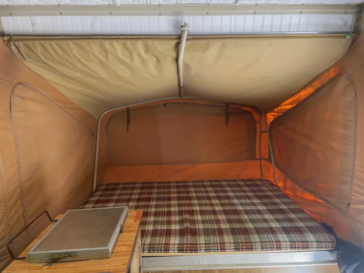 Cozy pop-up RV rental interior with plaid bed & small counter. Perfect for camping adventures.. Coleman Other 1983