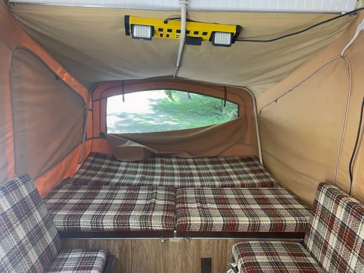 Plaid beds and seating fill this pop-up RV rental interior, offering a cozy retreat with a nature view.. Coleman Other 1983