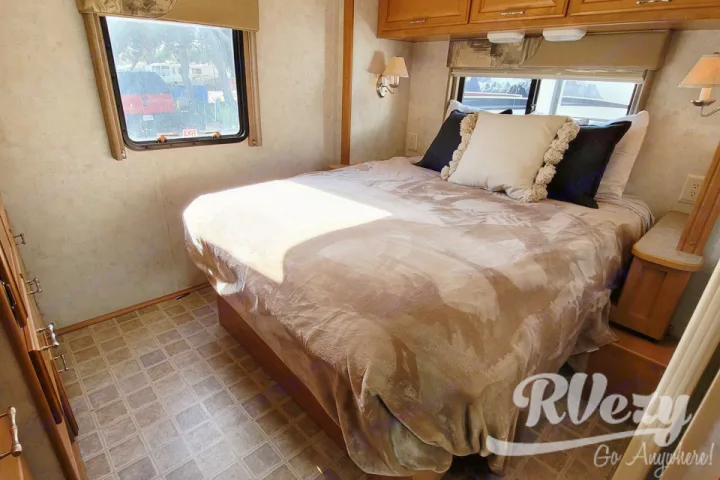 Cozy RV rental bedroom with queen bed, windows, and warm sunlight. Perfect for your next adventure!. Winnebago Chalet 2007