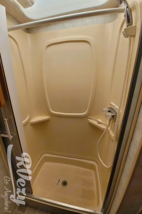 Inside an RV rental shower: Beige, compact enclosure with a visible drain and shower head fixture.. Winnebago Chalet 2007