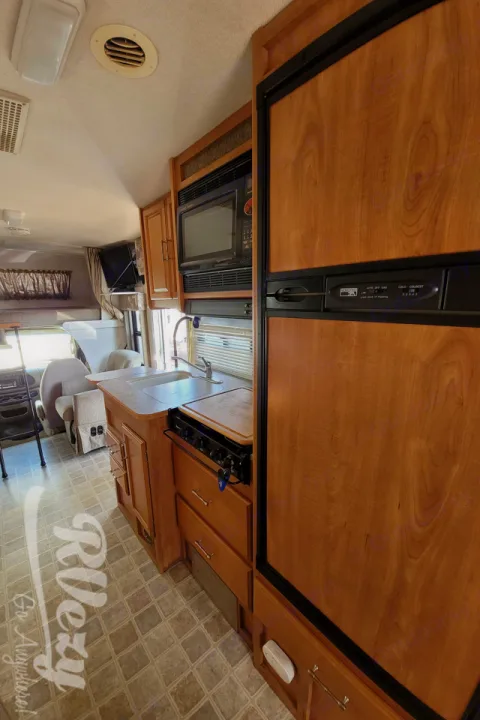 RV rental interior: full kitchen with wood cabinets, featuring a refrigerator, microwave, sink, and stovetop.. Winnebago Chalet 2007