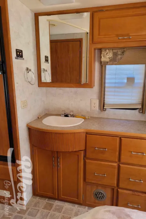 RV rental bathroom interior: wood cabinets, countertop, sink, mirror, & window. Compact & functional space.. Winnebago Chalet 2007
