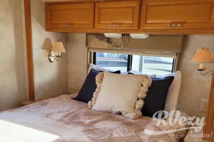 RV rental bedroom interior: a cozy bed with pillows, wall sconces, overhead storage, and a window view.. Winnebago Chalet 2007