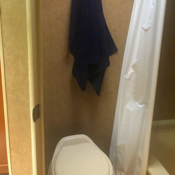 Interior of an RV rental bathroom, featuring a white toilet, blue towel, and shower curtain.. Forest River Cherokee 2014