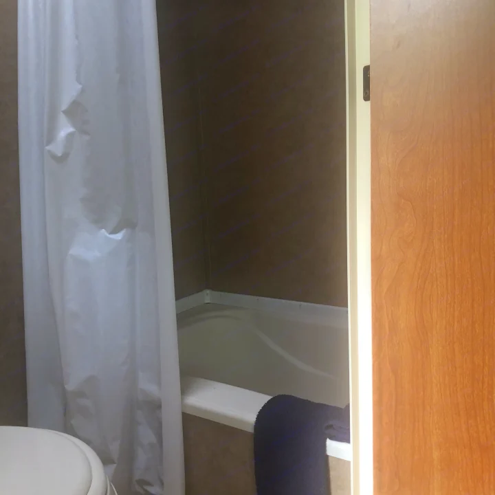 RV rental bathroom: white shower curtain, compact tub, partial toilet, wooden door, dark towel.. Forest River Cherokee 2014