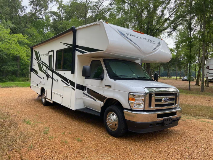 White Coachmen Freelander RV rental on gravel at a wooded campsite, ready for your outdoor travel and leisure adventures.. Forest River Coachmen Freelander Premier 2022
