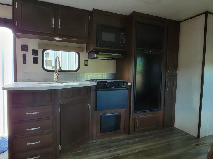 Spacious RV rental kitchen featuring dark wood cabinets, modern appliances including a microwave, stove, and refrigerator, with a sink and ample counter space.. Jayco Jay Flight 2020