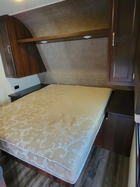 RV rental interior: bedroom view with a patterned mattress on the bed, dark wood cabinetry, and wall panels. Ideal for trips.. Jayco Jay Flight 2020