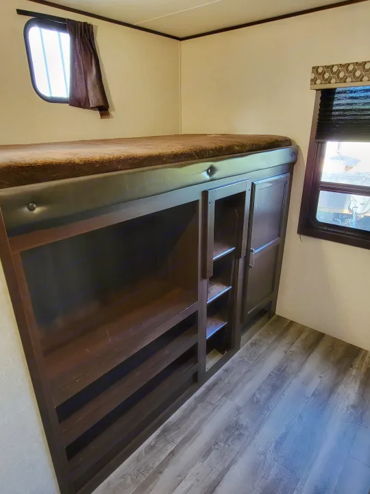 RV rental bedroom interior: dark wood bed frame with integrated storage shelves, window, and wood-look flooring.. Jayco Jay Flight 2020
