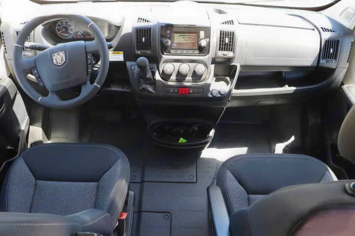 RV rental van's cockpit showing steering wheel, dashboard display, gear shifter, and front seats.. Winnebago Solis 2022