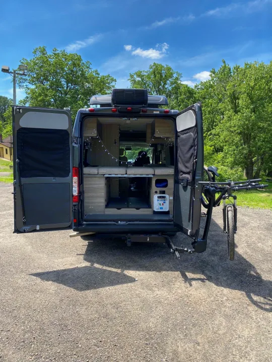 This **RV rental** showcases its open rear doors revealing a custom interior, power station, and bike rack with a mountain bike.. Winnebago Solis 2022