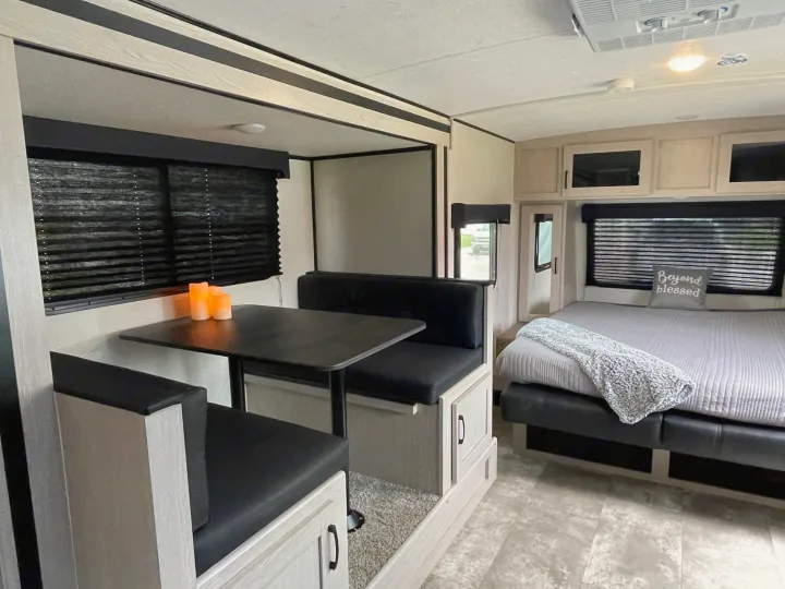 Modern RV rental interior with light wood, black accents, a cozy dinette, and comfortable bed.. Coachmen Apex 2022