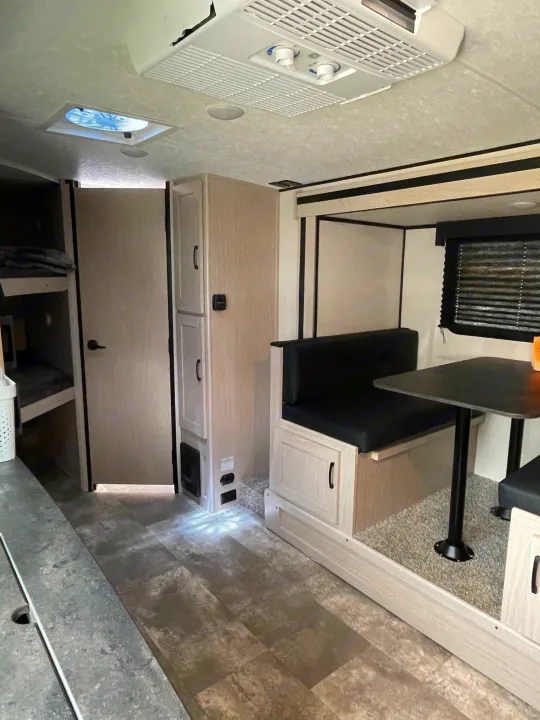 RV rental interior: light wood dinette with black cushions, bunk beds, and a clean, functional layout for travel.. Coachmen Apex 2022