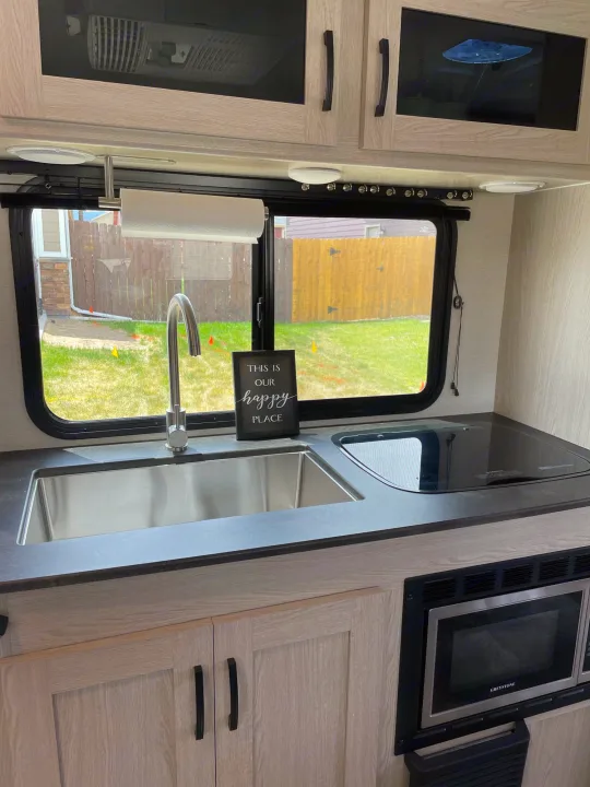 Stylish RV rental galley showcasing a stainless sink, built-in cooktop, microwave, and light wood cabinets.. Coachmen Apex 2022