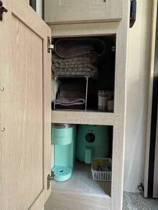 RV rental organized kitchen cabinet with coffee maker, air fryer, towels, and cleaning supplies for convenient travel.. Coachmen Apex 2022