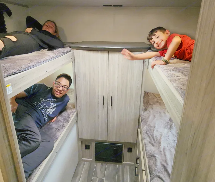Three people lounging in the bunk beds of an RV rental, a comfy space for family camping trips and relaxation.. Keystone RV Passport SL 2022