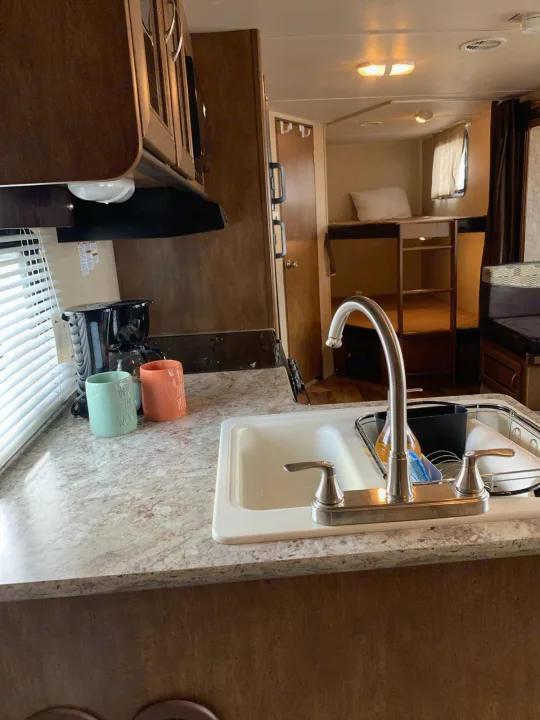 RV rental interior: A compact kitchen with sink, coffee maker, and mugs, opening to bunk beds in the background.. Forest River Wildwood X-Lite 2016