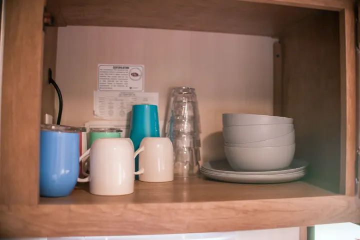 Inside an RV rental's organized cabinet, featuring colorful mugs, clear cups, grey bowls, and plates.. Gulf Stream Cruiser 2017