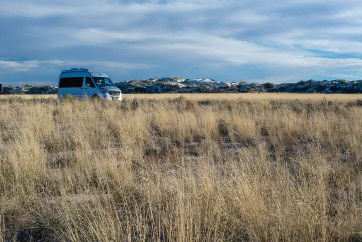 Experience nature: silver RV rental parked in a golden grass field near white dunes under a cloudy sky, ideal for camping.. Airstream Interstate 2020