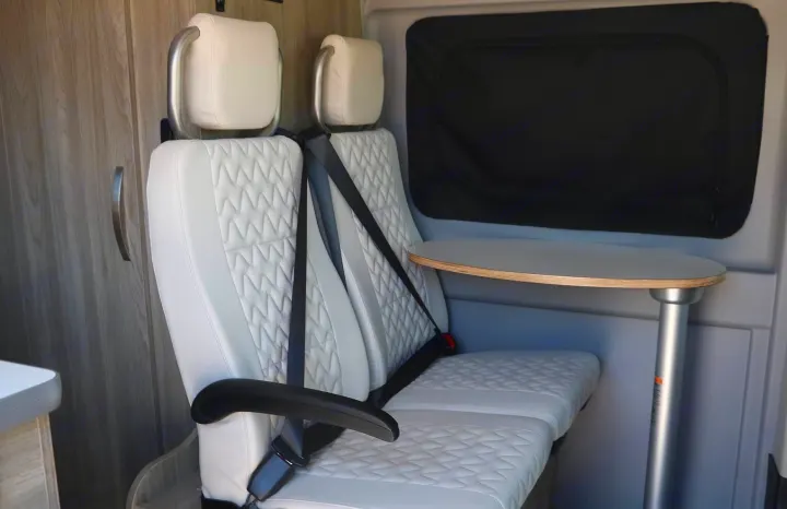 Modern RV rental interior features comfy quilted seats, seatbelts, and a round dining table with window privacy.. Winnebago Solis 2022