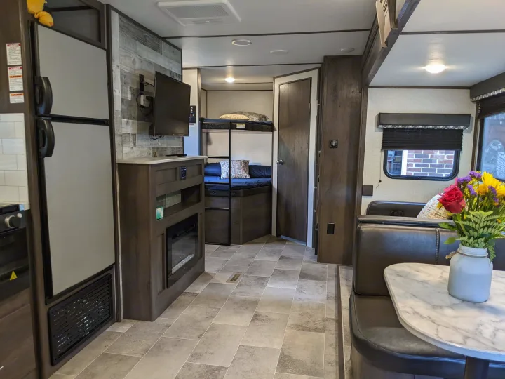 RV rental interior features a dinette with a floral centerpiece, compact kitchenette, TV, fireplace unit, and cozy bunk beds.. Dutchmen Coleman Light 2021