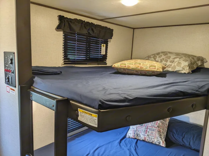 RV rental interior showing comfortable upper and lower bunk beds, with a window and control panel.. Dutchmen Coleman Light 2021
