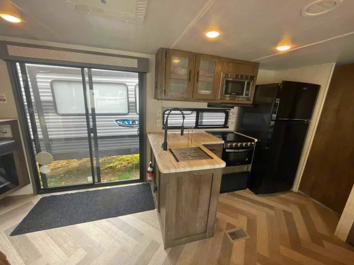 Step inside this RV rental's modern kitchen featuring a sink, appliances, herringbone floor, and a view through the glass door.. Salem 36VBDS 2021
