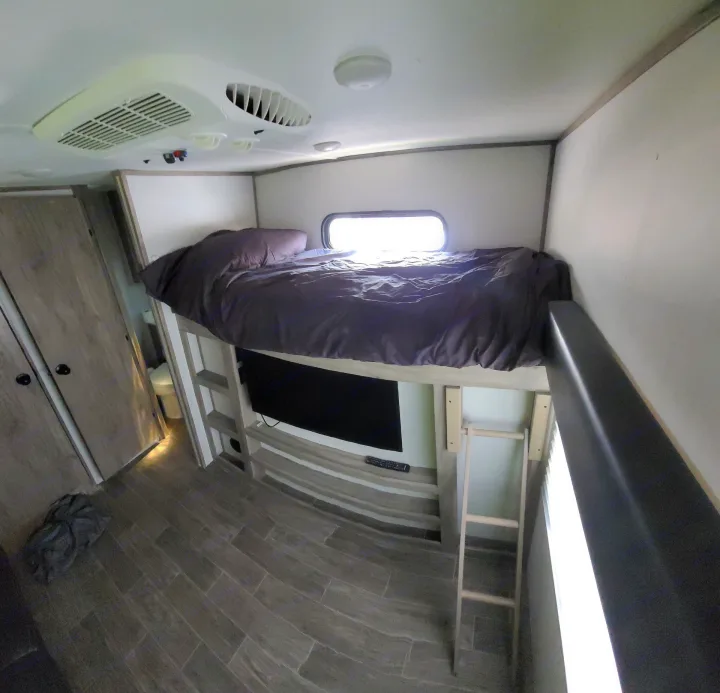Inside an RV rental: a cozy bunk bed with TV below, AC overhead, and a nearby bathroom, perfect for road trips.. Forest River Cherokee Alpha Wolf 2021