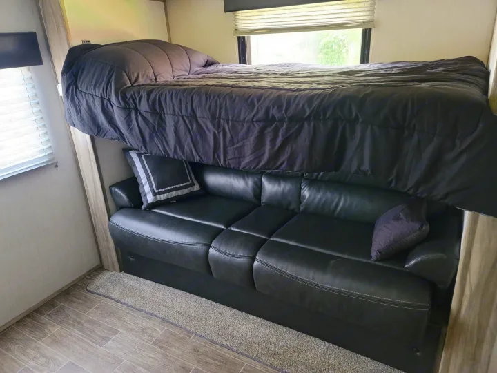 Dark bunk bed over a black sofa in an RV rental, highlighting efficient use of space for travel.. Forest River Cherokee Alpha Wolf 2021