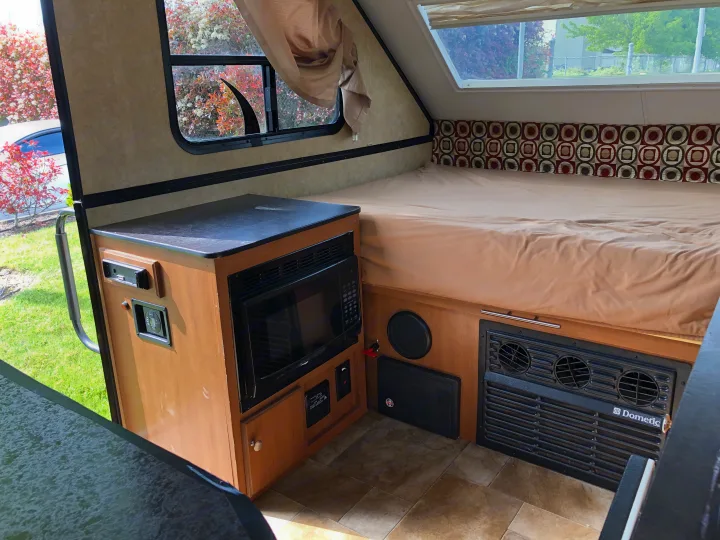 Compact A-frame RV rental interior with a cozy bed, microwave, and Dometic furnace/vent. Tiled floor and window views.. Starcraft Comet 2015