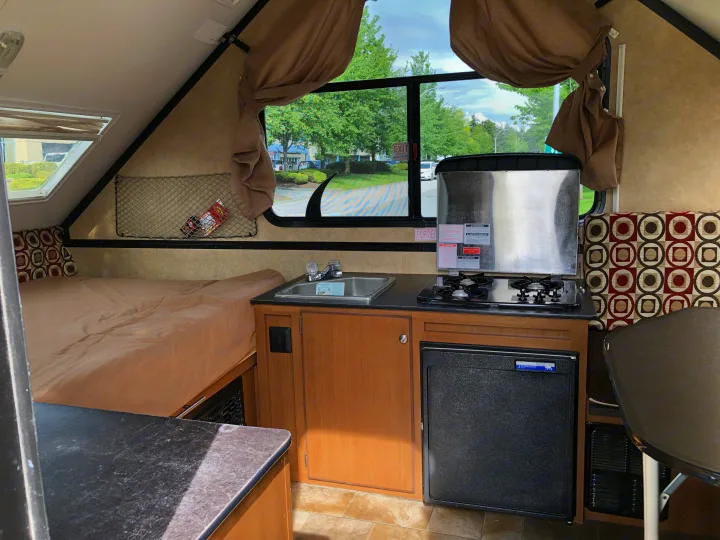 Cozy RV rental interior featuring a compact kitchen with sink and stove, sleeping area, and dinette table.. Starcraft Comet 2015