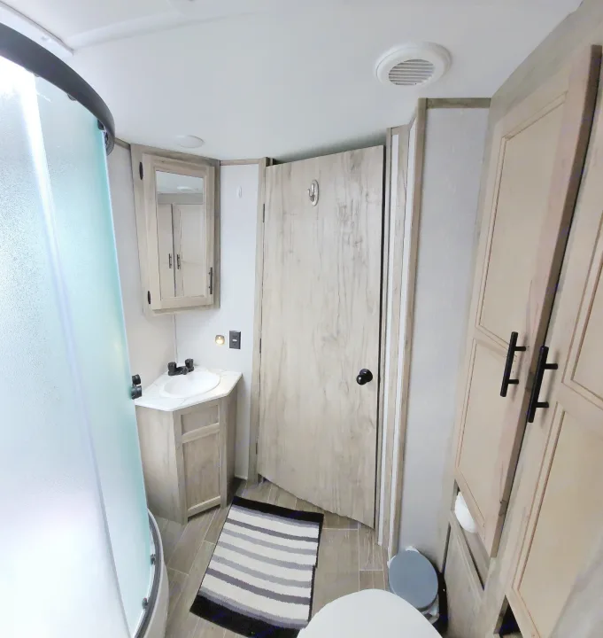 Compact RV rental bathroom featuring a glass shower, vanity sink, mirror, toilet, and light wood cabinetry.. Forest River Cherokee Alpha Wolf 2021