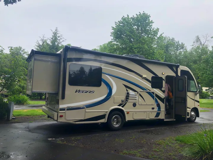 This beige Vegas RV rental motorhome is parked at a campsite with its rear slide-out extended and door open.. Thor Vegas 2017