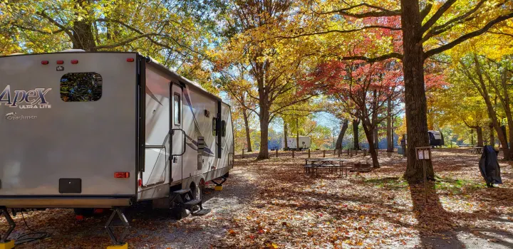 An RV rental, an Apex Ultra Lite travel trailer, is parked at an autumn campground, surrounded by golden and red fall foliage.. Coachmen Apex 265rbss 2019