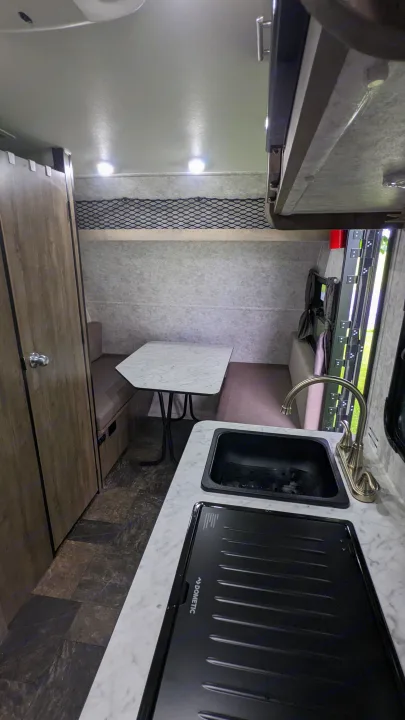 RV rental interior: compact kitchen (sink, Dometic stovetop), dining area with table/benches, and storage net. Great for travel.. Prolite RV Evasion 16 2022