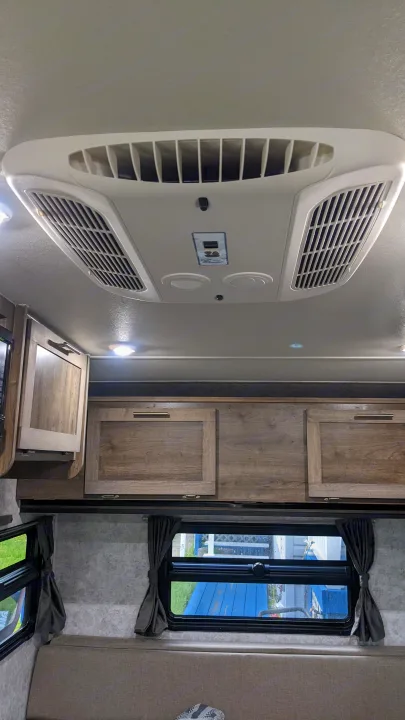 Inside an RV rental: overhead AC unit, wooden storage cabinets, and bright windows with tie-back curtains above a comfortable bench.. Prolite RV Evasion 16 2022