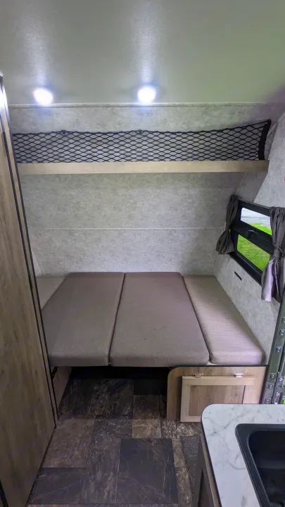 RV rental interior: A versatile bed/seating area, overhead storage net, window, and partial sink are visible. Ready for adventure!. Prolite RV Evasion 16 2022
