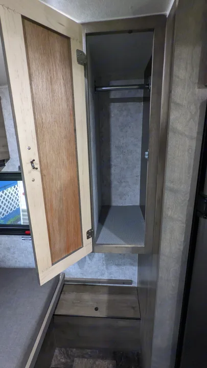 RV rental wardrobe: Open light wood closet with a metal hanging rod and lower shelf for compact storage.. Prolite RV Evasion 16 2022