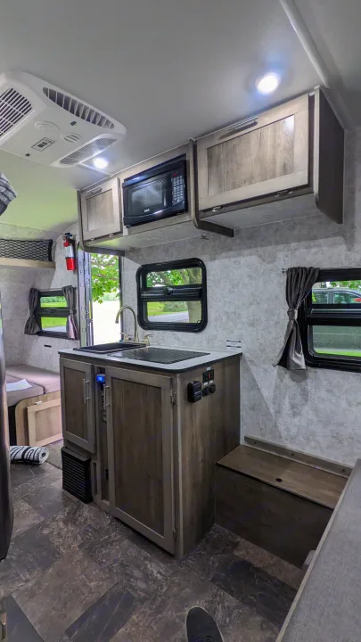 RV rental interior: A compact kitchen with sink, microwave, and cabinets, plus dinette, and overhead AC unit.. Prolite RV Evasion 16 2022