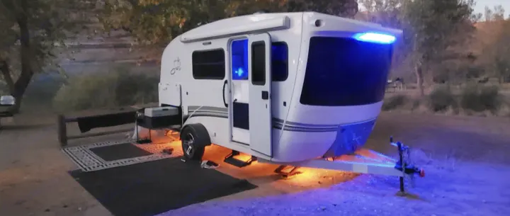 Night camping in a lit-up travel trailer RV rental, featuring blue and orange underglow lights at a peaceful site.. Intech Sol Horizon Rover 2022