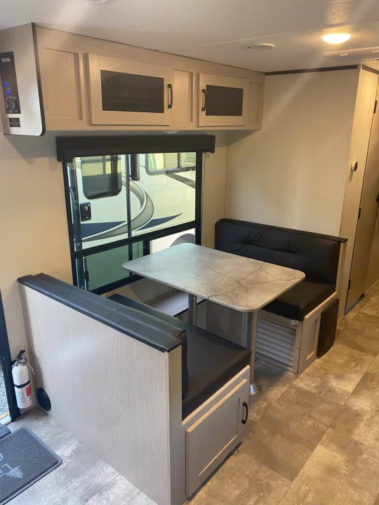 Spacious RV rental dinette area featuring a light wood table, black cushioned seating, overhead cabinets, and large window.. Forest River two bedroom Apex ultralite 2022