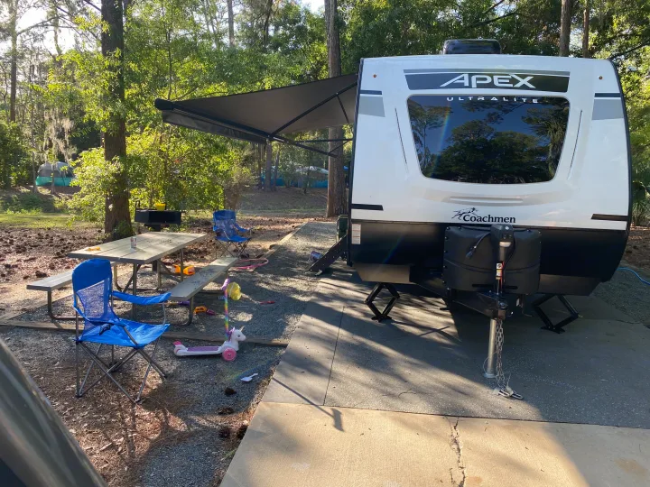 Perfect day at a wooded campsite with an Apex Ultralite rv rental, picnic table, and kids' toys. Great for families!. Forest River two bedroom Apex ultralite 2022