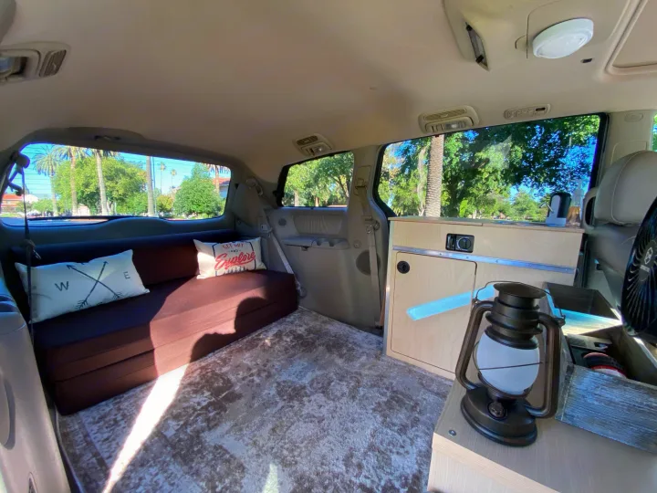 This customized van interior, ideal for an RV rental, showcases a comfy bed, storage, and homey touches for road trips.. Custom Camper 2004