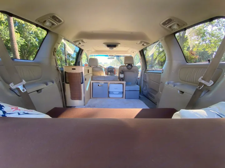 This **RV rental** features a cozy minivan camper setup, showcasing a bed and customized storage for travel and camping adventures.. Custom Camper 2004
